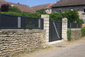 Clôture et portail aluminium gris anthracite installés sur un muret en pierre devant une maison traditionnelle.