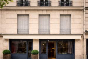 Persiennes métalliques accordéon gris clair sur façade haussmannienne à Paris.