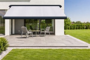 Store banne coffre intégral à toile claire ombrageant une terrasse carrelée devant une maison contemporaine.