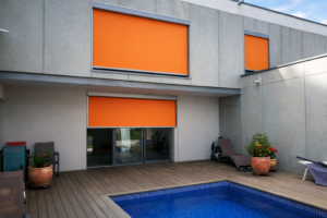 Stores verticaux screen orange sur façade moderne, au-dessus d’une terrasse bois avec piscine.